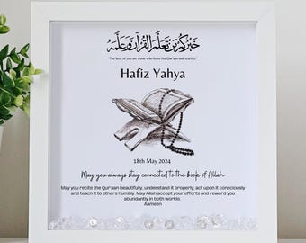 May include: A white framed print with a black and white illustration of an open Quran on a stand with prayer beads. The text reads "The best of you are those who learn the Quran and teach it."  "Hafiz Yahya"  "18th May 2024"  "May you always stay connected to the book of Allah"  "May you recite the Quran beautifully, understand it properly, act upon it consciously and teach it to others humbly. May Allah accept your efforts and reward you abundantly in both worlds. Aameen"