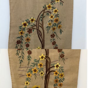 May include: A beige embroidered wall hanging with a brown tree with yellow and green flowers. A person in a blue and red patterned shirt is standing under the tree.