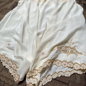 May include: Cream-coloured vintage bloomers with a high waist and a delicate, flowing fabric. The bloomers feature intricate floral embroidery and a scalloped lace trim in a warm, golden hue, adding a touch of vintage charm.