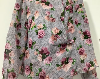 May include: A light purple blouse with a floral print featuring pink and purple roses. The blouse has a high neck and long sleeves.