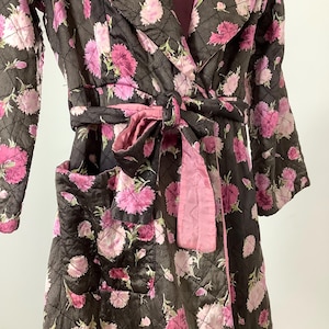May include: A quilted robe with a floral print in shades of pink and brown. The robe has a shawl collar, long sleeves, and a tie belt. It features a patch pocket on the left side.
