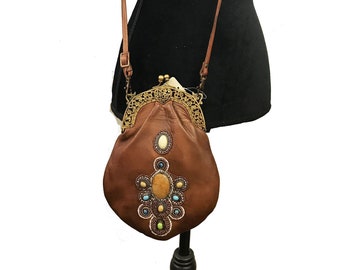 May include: A brown leather purse with a metal clasp and colourful gemstone embellishments. The purse has a long strap for wearing it as a crossbody bag.