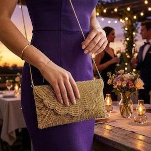 May include: A gold beaded clutch bag with a scalloped flap closure and a thin gold chain shoulder strap. The rectangular bag features an intricate, textured pattern of small gold beads covering the entire exterior surface, including the flap.