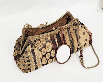 May include: A patterned clutch bag in brown, tan, and gold tones. It has a metal clasp, a small attached mirror, and a beaded chain handle. The bag's exterior features a textured fabric design. The interior is a dark brown fabric.