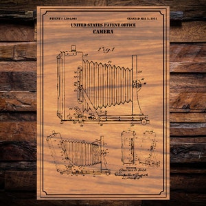 May include: A vintage black and white line drawing of a camera patent. The patent is for a camera with a bellows system and is titled "United States Patent Office Camera". The patent number is 1,801,081 and was granted on May 5, 1931.