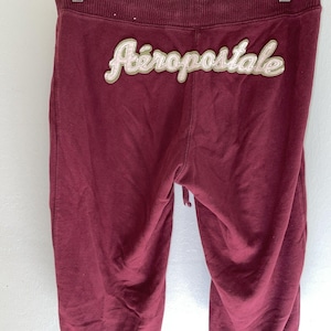 May include: Maroon Aeropostale sweatpants with a drawstring waist. The brand name is embroidered in a cream-colored script across the back. The pants are made of a soft, comfortable material.