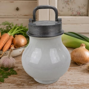 May include: A white ceramic storage jar with a rounded body and a dark grey metal lid featuring a vertical handle. The jar has a smooth, glossy finish and a wide base, providing a stable container for kitchen storage needs in a home setting.