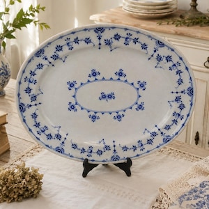 Peut inclure: Un plat de service ovale en céramique présentant une base blanche avec des motifs complexes de fleurs et de vignes bleues. Le design comprend une bordure ovale centrale avec de petits motifs floraux et un bord décoratif.