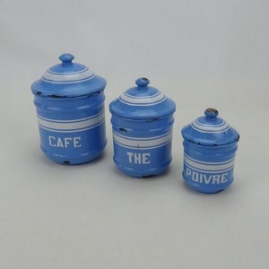 May include: Three blue and white enamel canisters with lids. The canisters are labeled "Cafe", "The", and "Poivre".