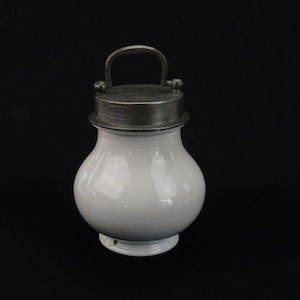May include: White ceramic jar with a silver lid and a handle. The jar has a rounded body and a small base.