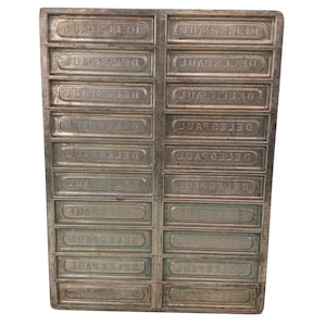 Puede incluir: Un molde rectangular de metal plateado con múltiples compartimentos rectangulares. Cada compartimento tiene el texto "DELESPAU" en relieve en una fuente curva. El molde parece ser vintage y tiene un aspecto ligeramente envejecido.