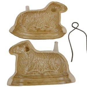 May include: Two tan ceramic lamb molds with detailed fur texture, and a metal wire clip. The molds are in the shape of a lamb, with a base and a small handle. The wire clip is used to hold the molds together.