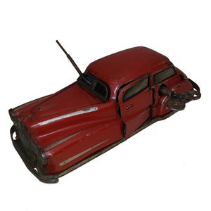 Peut inclure: Voiture jouet rouge à remonter avec une clé sur le côté. La voiture a des rayures blanches et un pare-brise noir.