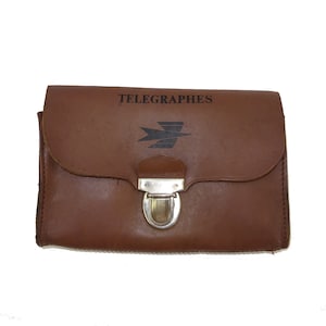 May include: A brown leather case with a silver clasp. The case has the words "TELEGRAPHES" and a stylized bird logo printed on the front.