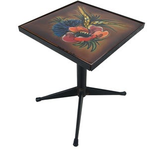 Op de afbeelding: Vierkante bijzettafel met een zwart metalen onderstel en een bloemenontwerp op het tafelblad. Het tafelblad heeft een bruine achtergrond met een rode klaproos, blauwe distel en tarwearen. De tafel is ongeveer 51 cm hoog.