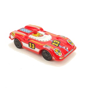 Könnte beinhalten: Ein rotes und weißes Spielzeug-Rennwagen mit der Nummer 13 an der Seite. Das Auto hat eine schwarze Fahrerfigur im Inneren und schwarze Räder.