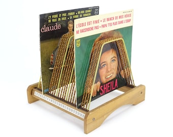 Può includere: Un porta dischi in legno con una griglia in filo d'oro contiene due dischi in vinile. Le copertine dei dischi mostrano immagini di Claude e Sheila, con testo in francese sulle copertine. Il supporto ha una base numerata.