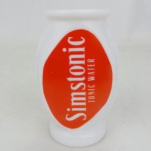 Può includere: Una bottiglia bianca di forma ovale con base arrotondata e collo stretto. La bottiglia presenta una grande etichetta arancione con la scritta "Simstonic TONIC WATER" in lettere bianche. La bottiglia ha una finitura liscia e lucida.