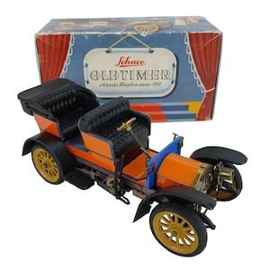 Könnte beinhalten: Ein Oldtimer-Modellauto von Schuco, Mercedes Simplex, in Orange, Schwarz und Gold. Das Modellauto hat ein schwarzes Cabrioverdeck und goldene Räder. Die Schachtel zeigt das Schuco-Logo und die Aufschrift "Oldtimer" und "Mercedes Simplex anno 1902".