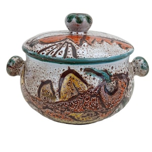 May include: A white ceramic mug with a black handle and the text "But First, Coffee" in a bold, black font. The mug is set against a blurred background, suggesting a cosy setting.