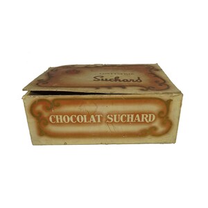 May include: A vintage cardboard box for  'Chocolat Suchard' with a brown and gold design. The box is open and the lid is slightly askew. The text 'Confiserie Suchard' is printed on the lid.