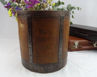 Può includere: Un secchio di legno vintage con fasce metalliche e le parole "Double Décalitre" stampate sul lato. Il secchio è marrone e ha un aspetto rustico. È pieno di un mazzo di fiori secchi.
