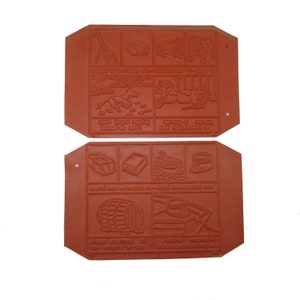 May include: Two red rubber stamps with raised images of animals, objects, and text. The top stamp has images of a giraffe, a dog, a horse, and a tree. The bottom stamp has images of a barrel, a can, a box, and a bowl. The text on the stamps is in a foreign language.