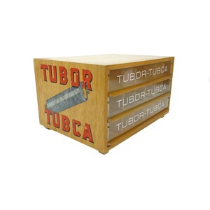 May include: A wooden box with three drawers, each labelled "Tubor-Tubca". The box has a red and white logo on the front that says "Tubor Tubca" and a picture of a spool of thread.