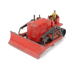 May include: Red toy bulldozer with a black blade and a small figure of a person in a yellow uniform sitting in the driver's seat.