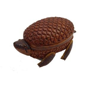 Könnte beinhalten: Eine kleine, braune, geflochtene Schachtel in Form einer Schildkröte mit einem Scharnierdeckel. Die Schachtel ist aus natürlichen Materialien gefertigt und hat ein rustikales, handgefertigtes Aussehen.