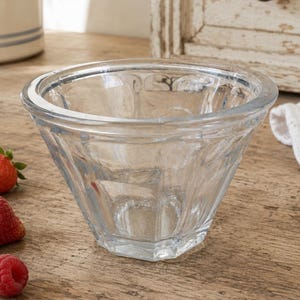 May include: A clear glass bowl with a faceted, multi-sided exterior design and a smooth, circular rim. The bowl features a wide opening that tapers down to a smaller, flat base, showcasing a transparent construction with subtle light reflections.