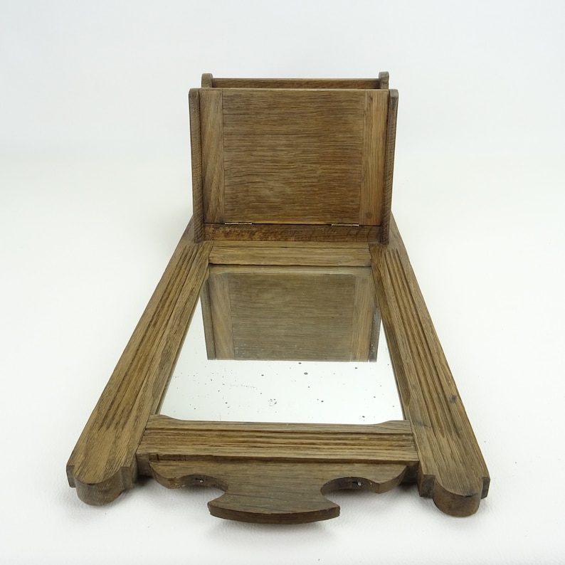 May include: A wooden wall-mounted mirror with a small shelf above it. The mirror is rectangular and has a simple frame. The shelf is also rectangular and has a slightly ornate design.