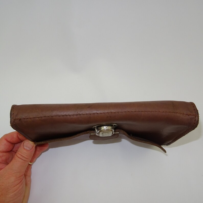 Może przedstawiać: Brązowy sk&oacute;rzany portfel z srebrnym zapięciem.