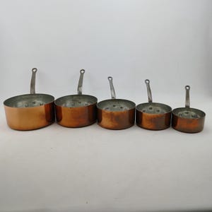 K&ouml;nnte beinhalten: Ein Set aus f&uuml;nf Kupfer-Kocht&ouml;pfen mit silberfarbenen Griffen. Die T&ouml;pfe sind unterschiedlich gro&szlig; und haben eine gl&auml;nzende Kupferau&szlig;enseite und eine silberne Innenseite. Jeder Topf hat einen kleinen Griff.