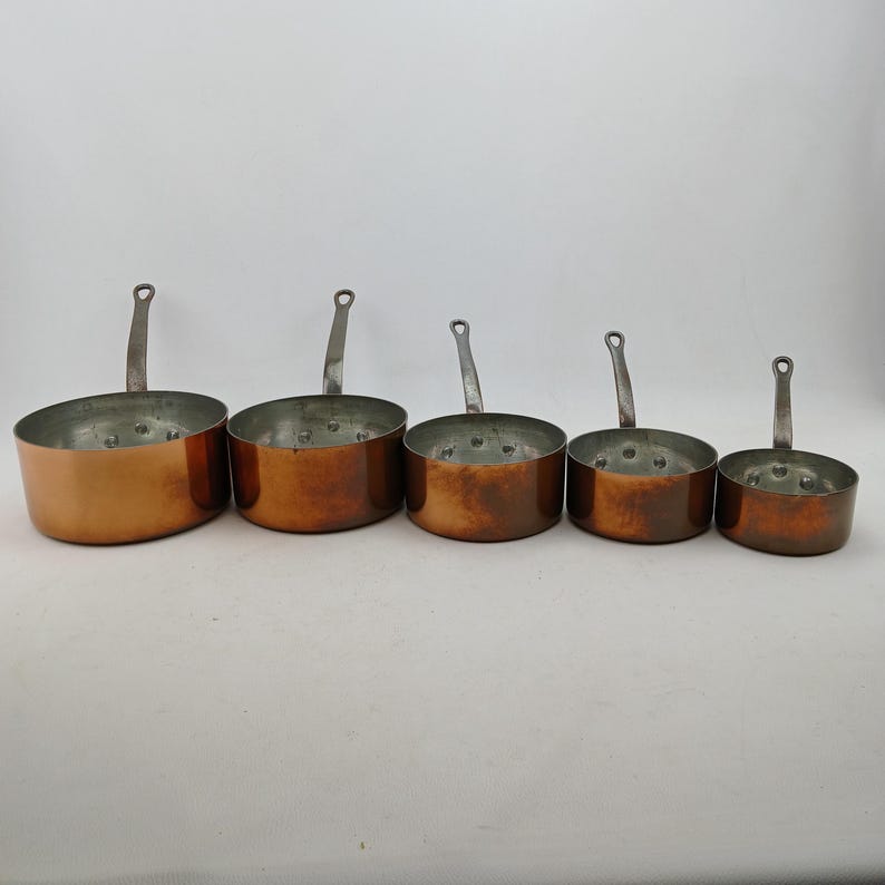 K&ouml;nnte beinhalten: Ein Set aus f&uuml;nf Kupfer-Kocht&ouml;pfen mit silberfarbenen Griffen. Die T&ouml;pfe sind unterschiedlich gro&szlig; und haben eine gl&auml;nzende Kupferau&szlig;enseite und eine silberne Innenseite. Jeder Topf hat einen kleinen Griff.
