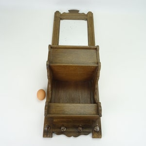 May include: A wooden wall-mounted shelf with a mirror, two shelves, and three hooks. The shelf is stained a dark brown color.
