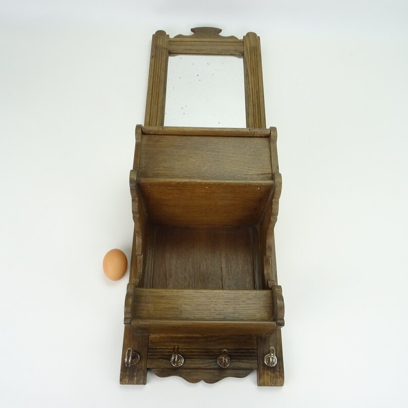 May include: A wooden wall-mounted shelf with a mirror, two shelves, and three hooks. The shelf is stained a dark brown color.