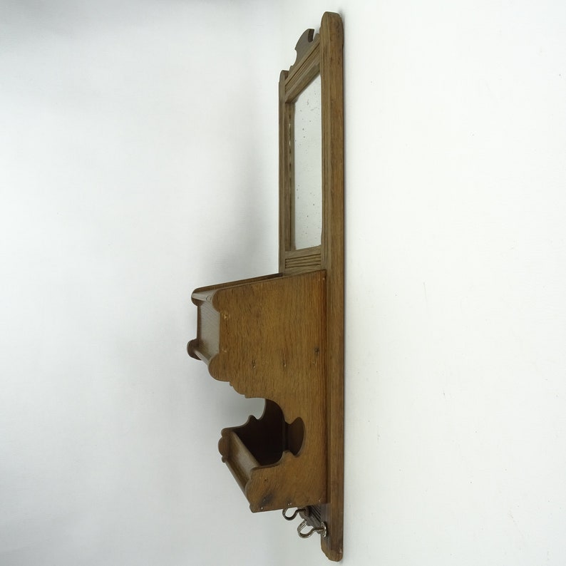 May include: A wooden wall-mounted mirror with two shelves and hooks underneath. The mirror has a simple frame and the shelves are unfinished.