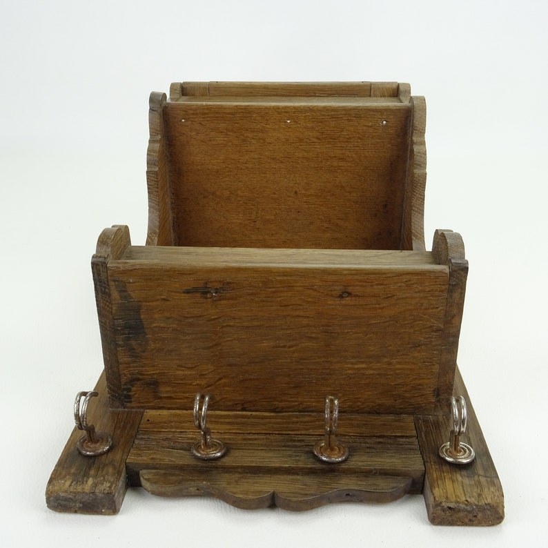 May include: A wooden wall-mounted key holder with a shelf and three hooks. The key holder is made of dark brown wood and has a rustic look.
