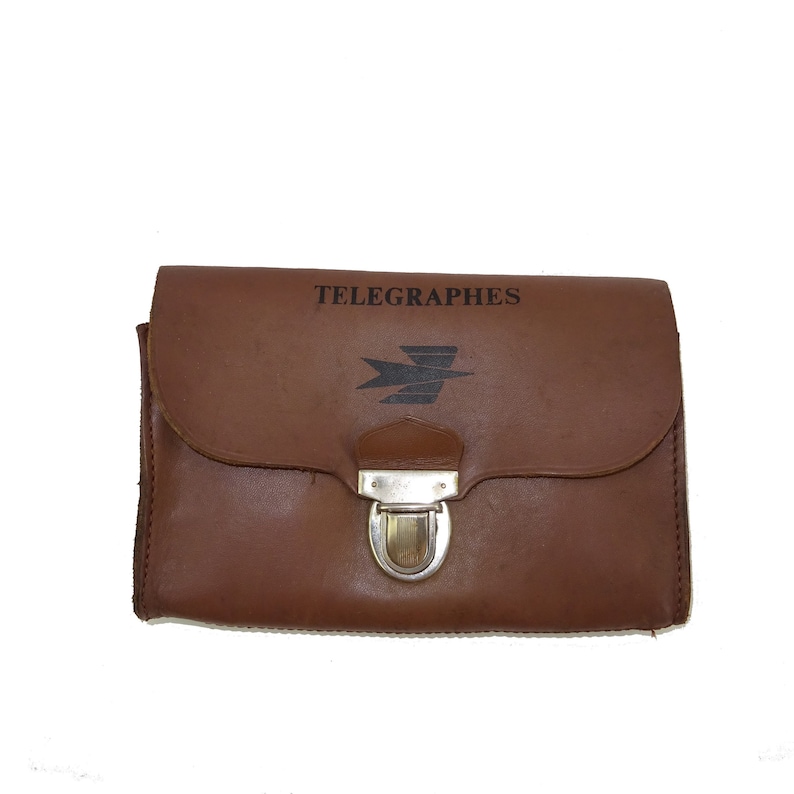 Może przedstawiać: Brązowa sk&oacute;rzana teczka z srebrnym zamkiem. Na przodzie teczki widnieje napis "TELEGRAPHES" i stylizowane logo ptaka.