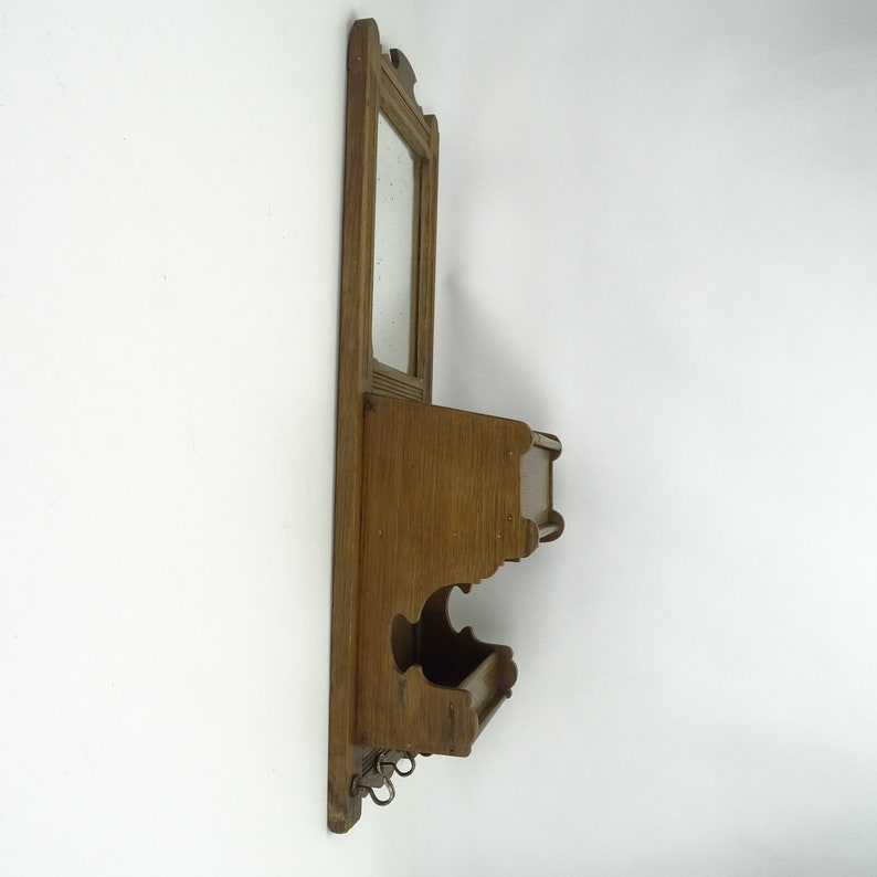 May include: A wooden wall-mounted shelf with a small mirror and two hooks. The shelf has a white painted surface and is decorated with carved details.
