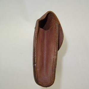 Może przedstawiać: Brązowa sk&oacute;rzana kabura z klapką. Wnętrze kabury jest widoczne i jest ciemnobrązowe.