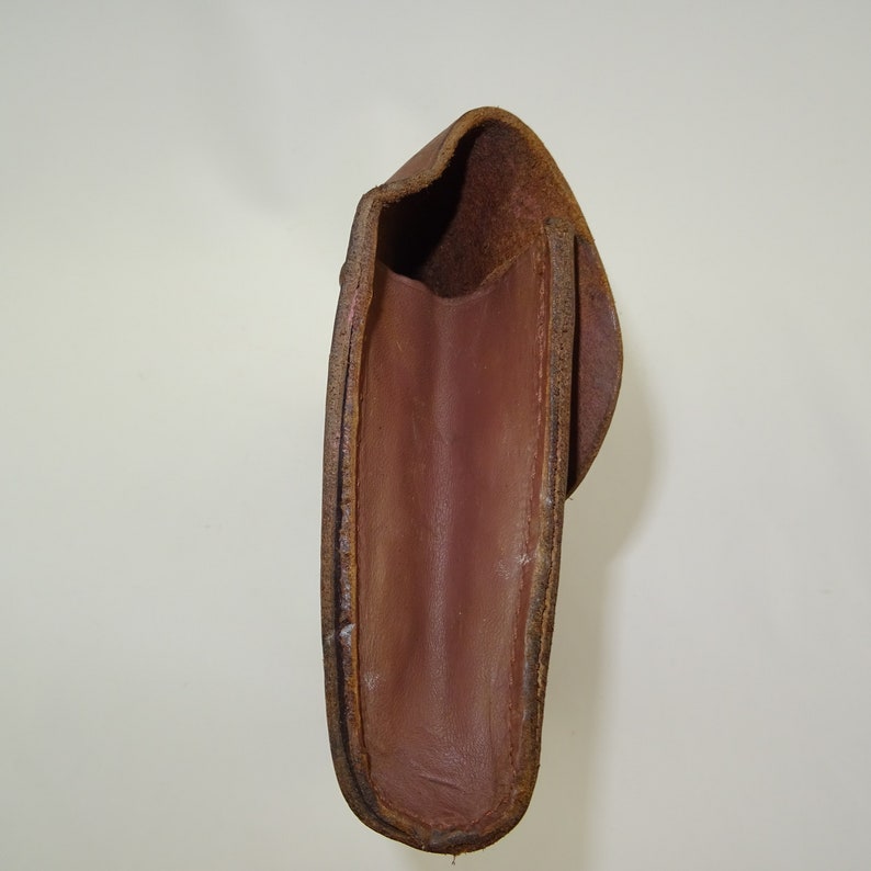 Może przedstawiać: Brązowa sk&oacute;rzana kabura z klapką. Wnętrze kabury jest widoczne i jest ciemnobrązowe.