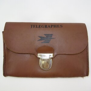Może przedstawiać: Brązowa sk&oacute;rzana teczka z metalowym zapięciem. Na przodzie teczki widnieje napis "TELEGRAPHES" i stylizowane logo ptaka.
