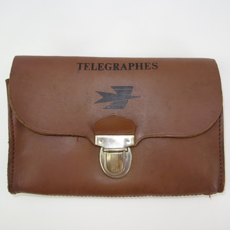 Może przedstawiać: Brązowa sk&oacute;rzana teczka z metalowym zapięciem. Na przodzie teczki widnieje napis "TELEGRAPHES" i stylizowane logo ptaka.