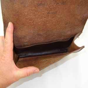 Może przedstawiać: Brązowa sk&oacute;rzana torebka z klapką. Torebka jest otwarta, a wnętrze wyłożone jest ciemnobrązową tkaniną. Torebka wykonana jest z miękkiej, elastycznej sk&oacute;ry.