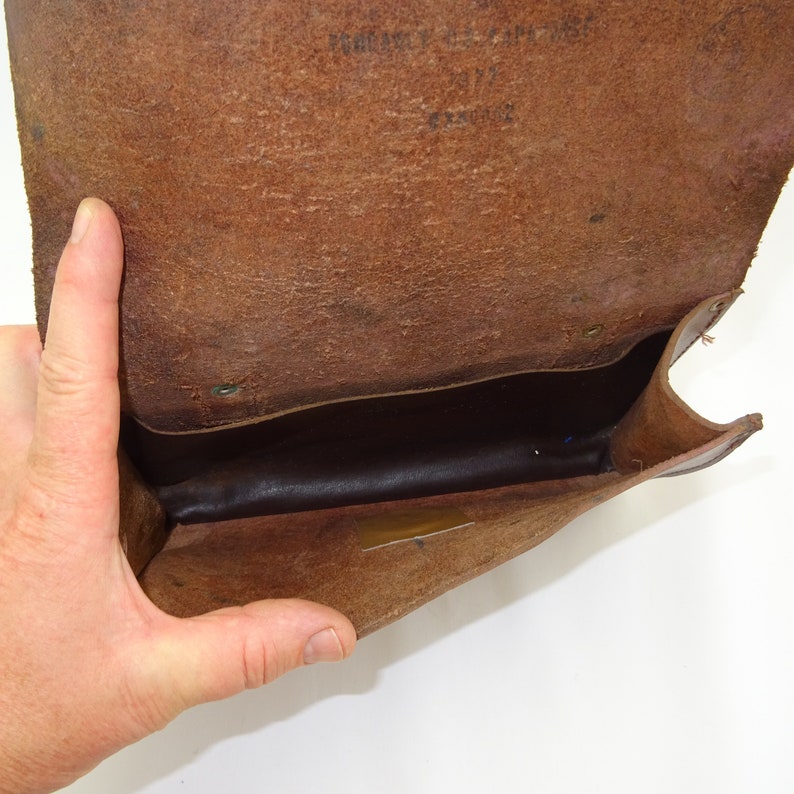 Może przedstawiać: Brązowa sk&oacute;rzana torebka z klapką. Torebka jest otwarta, a wnętrze wyłożone jest ciemnobrązową tkaniną. Torebka wykonana jest z miękkiej, elastycznej sk&oacute;ry.