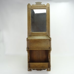 May include: A wooden wall-mounted mirror with a shelf and two compartments below. The mirror has a simple frame and the wood is a light brown color.