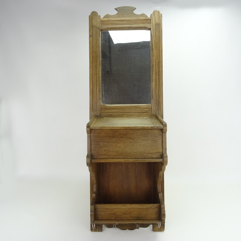 May include: A wooden wall-mounted mirror with a shelf and two compartments below. The mirror has a simple frame and the wood is a light brown color.