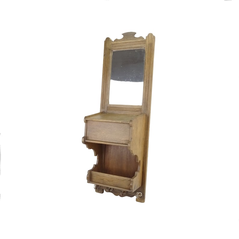 May include: A wooden wall-mounted shelf with a mirror, a small drawer, and a shelf with hooks. The shelf is made of light brown wood and has a simple design.